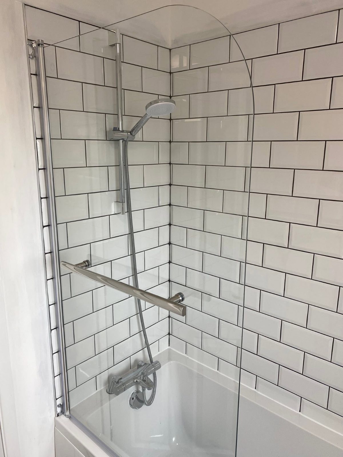 White metro tiling around a bath with a curved shower screen