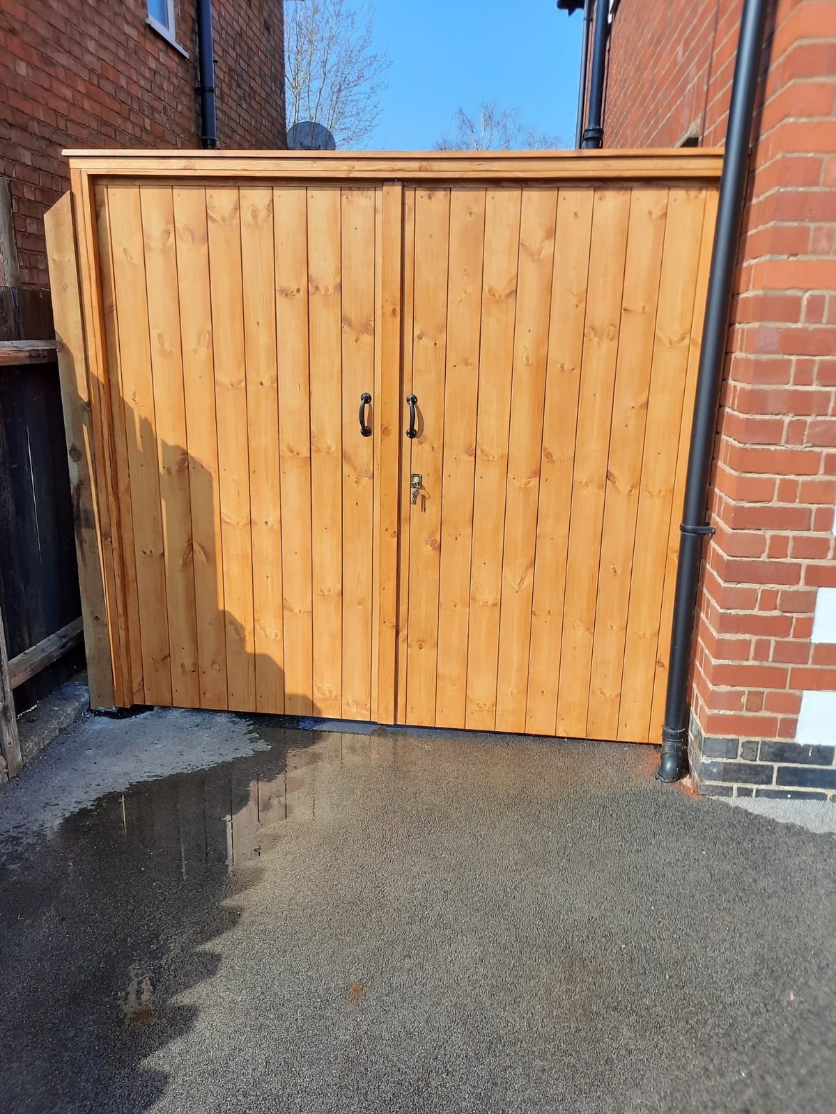 Stained timber bin store with double doors and black handles beside a house wall
