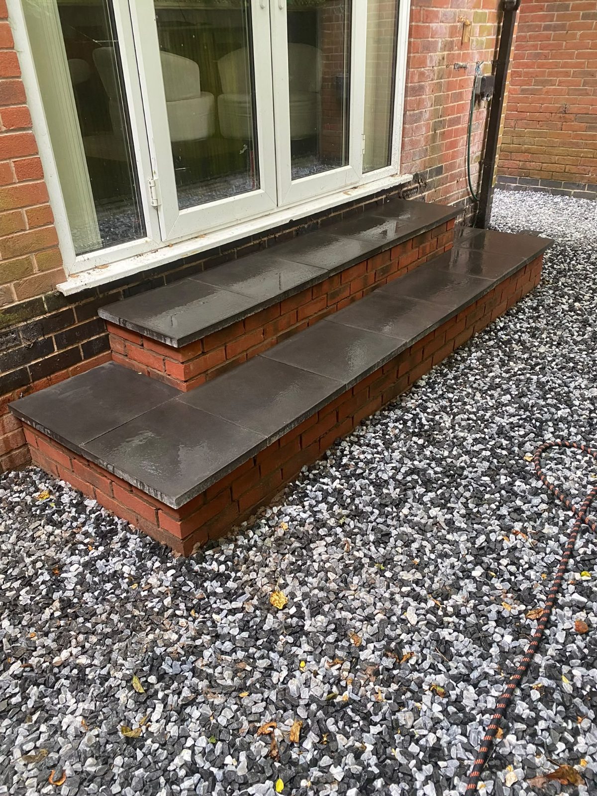 Finished brick and slate steps running below a window, gravel laid up to them