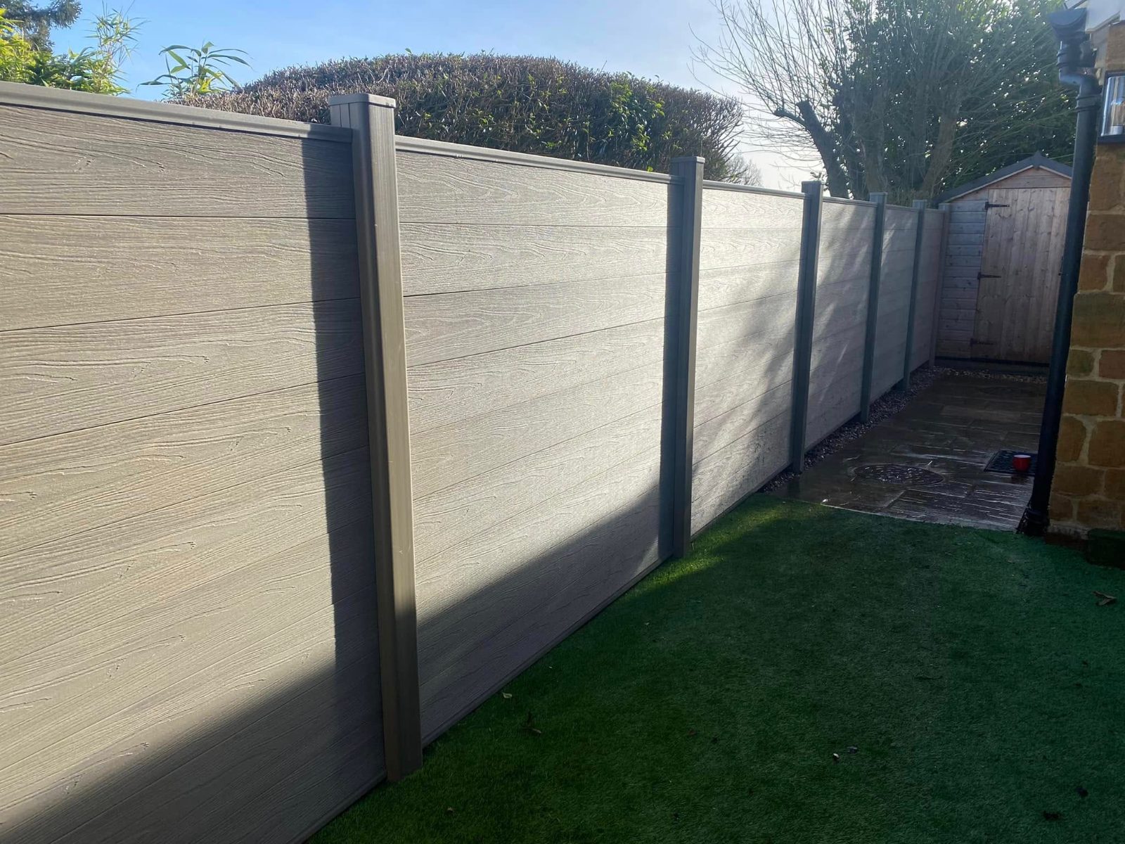 Long run of grey composite fencing in low sun