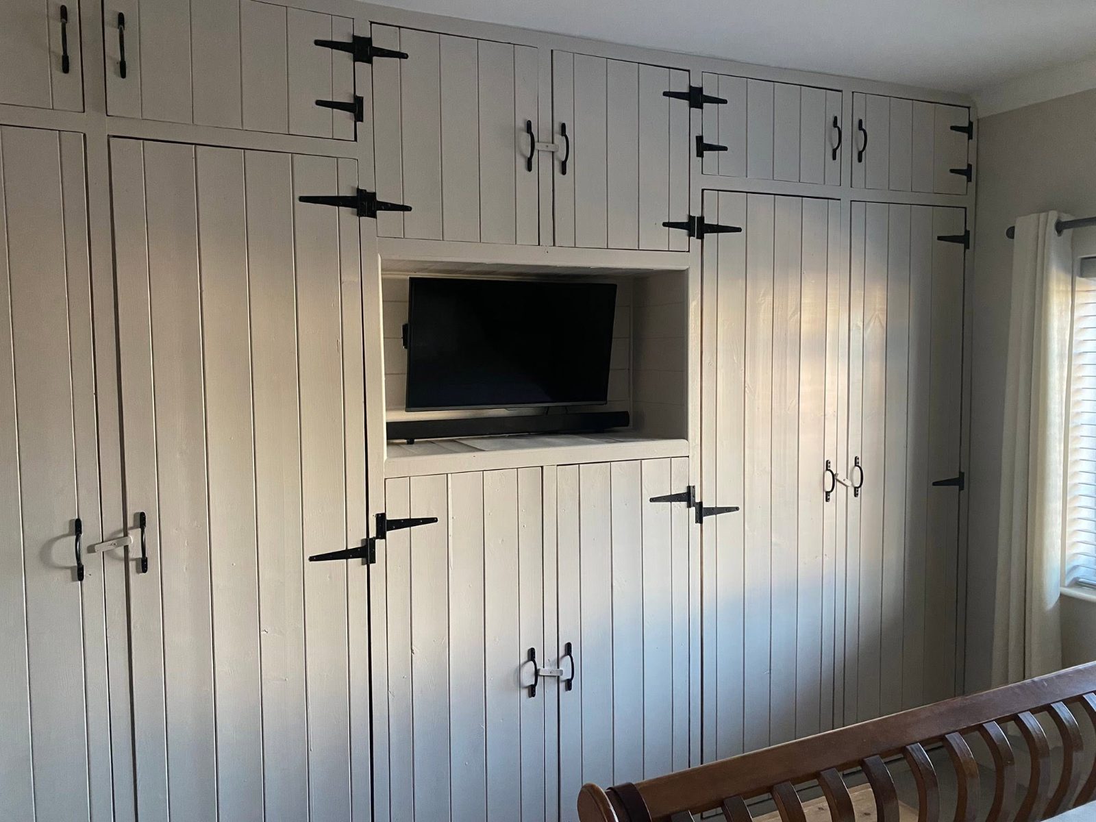Wall of fitted panelled wardrobes with black forged hinges and a recessed TV