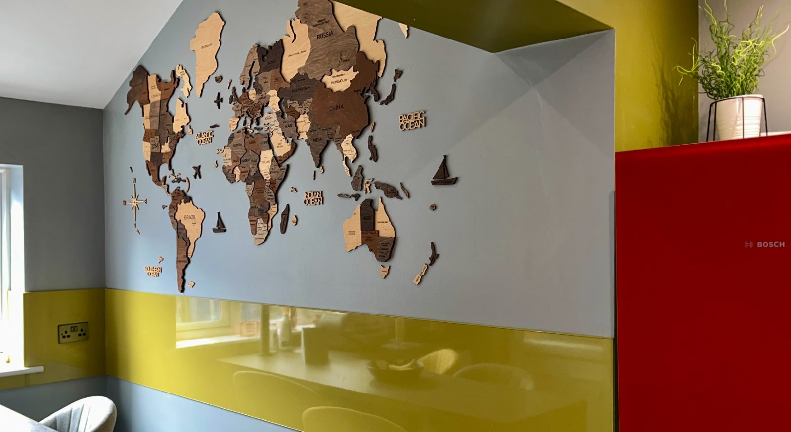 Kitchen wall with a layered wooden world map above a yellow splashback