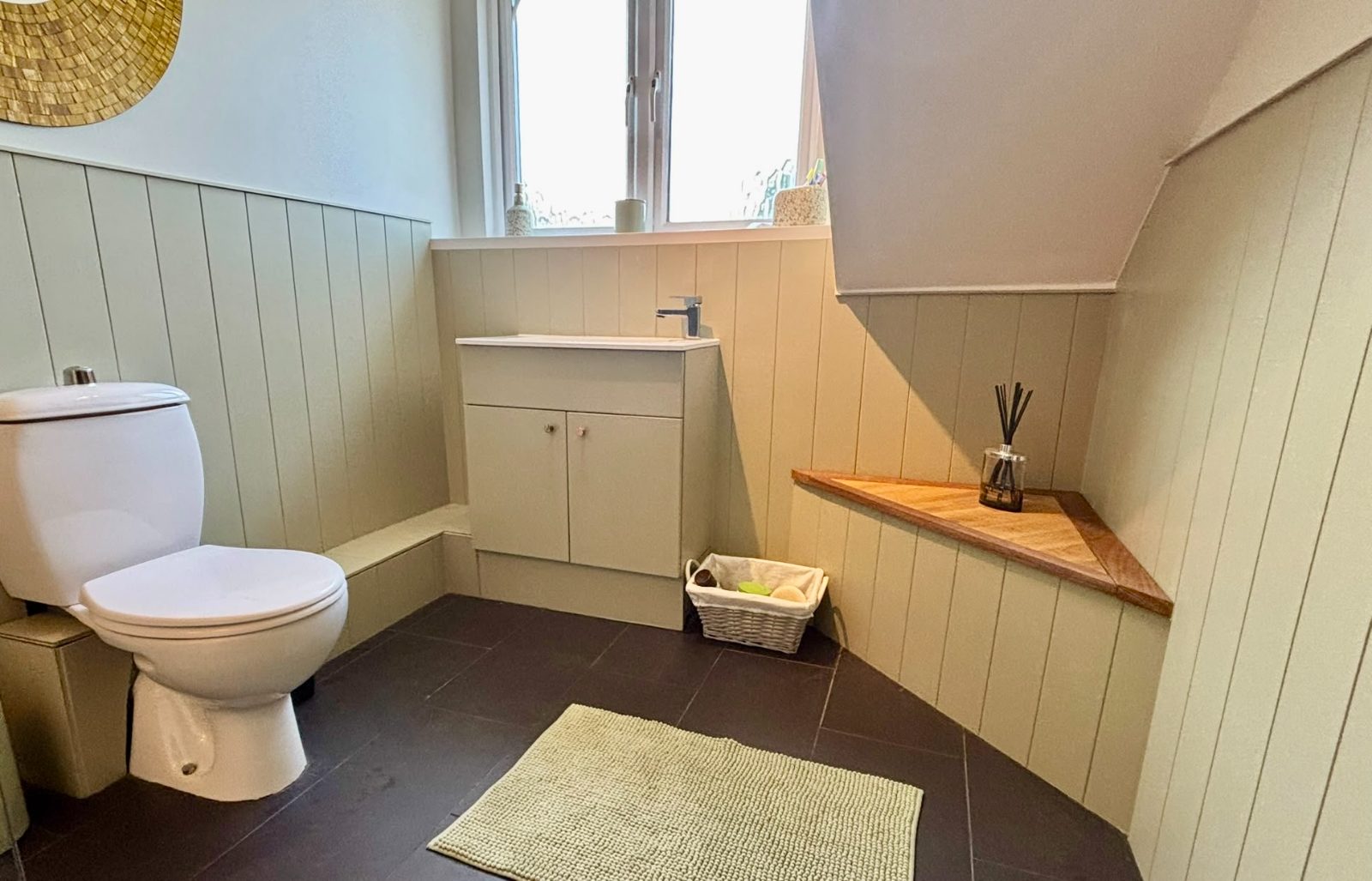 Cloakroom in sage green tongue and groove panelling with a handmade hardwood corner shelf under the stairs