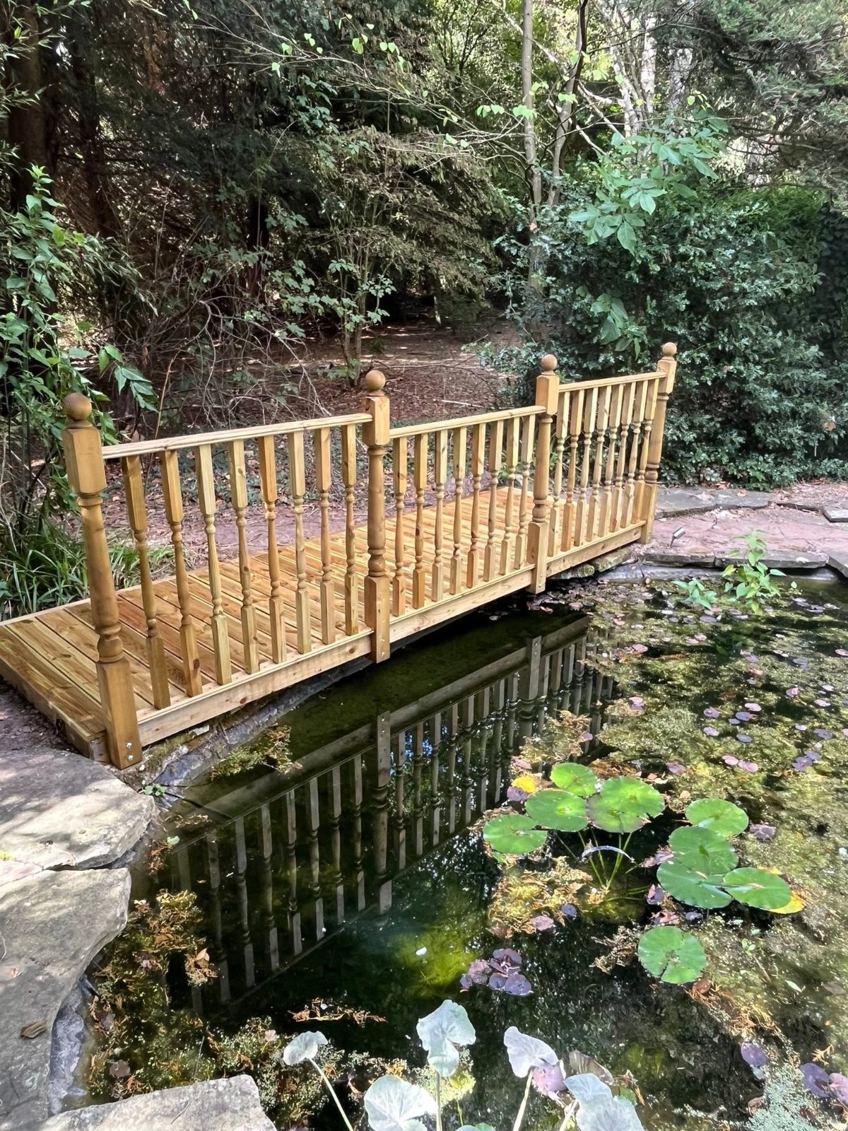Timber bridge with turned spindles crossing a lily pond