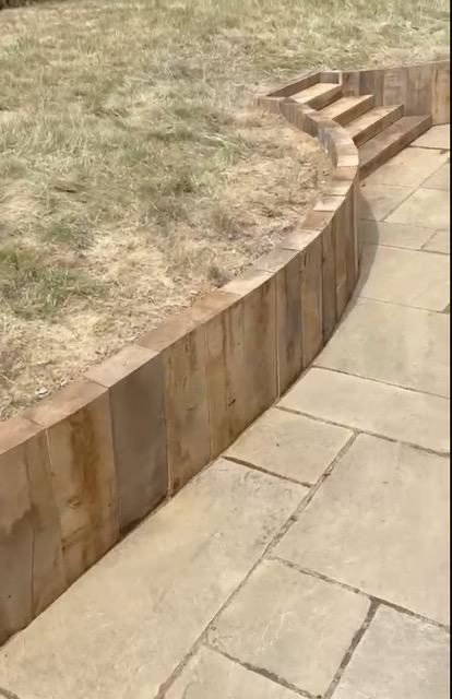 Curved oak sleeper retaining wall above sawn stone paving in the sun