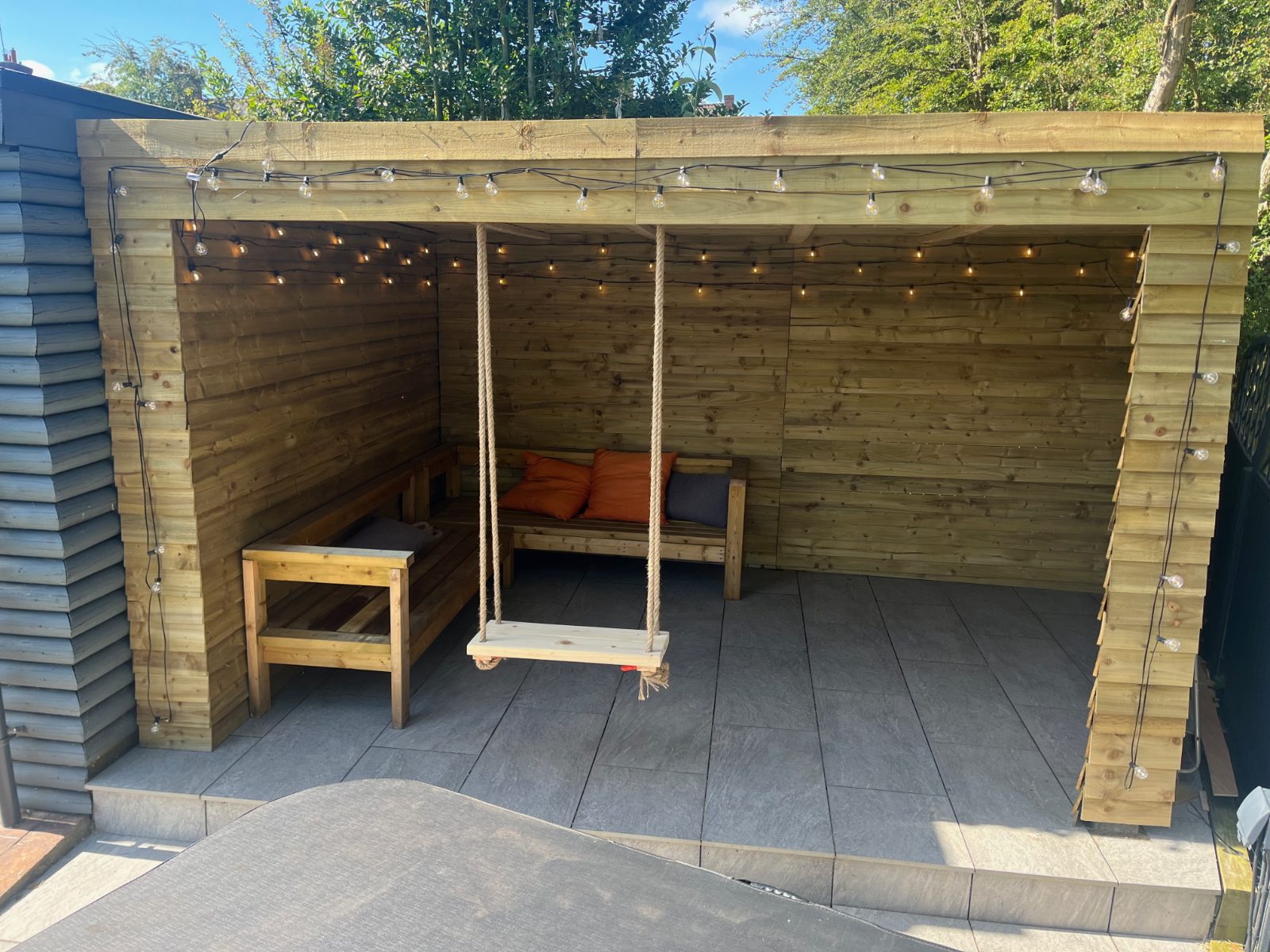 Timber garden shelter with festoon lights, bench seating and a rope swing