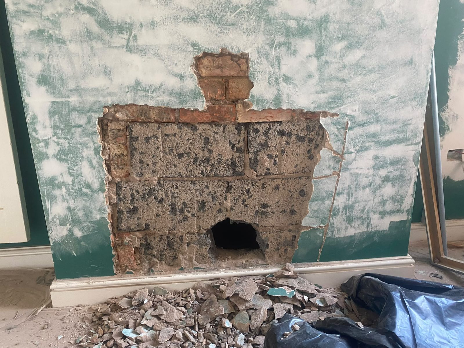 Blocked-up chimney breast opened back to bare brick with rubble on the floor